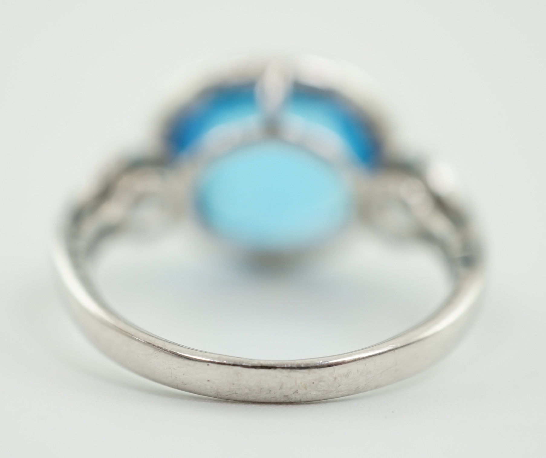 A modern 18ct white gold and facetted oval cut blue topaz set dress ring, with diamond chip set border and shoulders